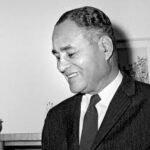 A black and photo of Ralph Bunche smiling while wearing a black suit.