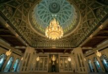 Tragic Mosque Shooting In Muscat, Oman: Six Dead, Including Police Officer Ornate interior of the Sultan Qaboos Grand Mosque in Muscat, Oman, featuring a large, intricate chandelier hanging from a beautifully patterned dome ceiling. The mosque’s architecture showcases detailed Islamic art and craftsmanship.