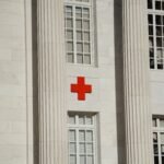 Exterior of a white marble building with a red cross symbol, representing humanitarian aid and emergency medical services.